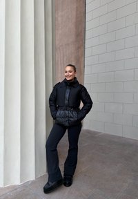 Czarna puchowa kurtka z paskiem w talii, z wysokim kołnierzem i dużymi kieszeniami. Połączona z dopasowanymi ciemnymi spodniami i masywnymi czarnymi butami.