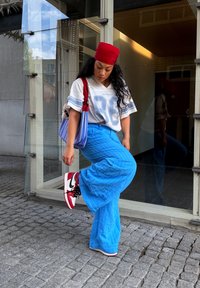 Γκρι και μπλε ριγέ oversized πουκάμισο από βαμβάκι, μπλε φαρδιά παντελόνια, κόκκινη κορδέλα, μαύρα και κόκκινα sneakers, πολύχρωμη ριγέ τσάντα.