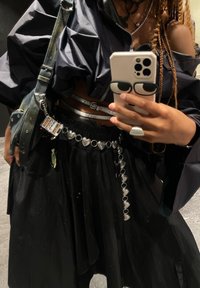 Zwarte oversized jas met opgezette schouders, gedragen over een rok. Zilveren hartvormige riem, reflecterende metallic tas en ringen.
