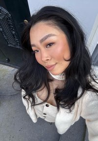 Pullover bianco con texture e grandi bottoni, indossato sopra un top a collo alto. La persona ha capelli neri mossi e uno sfondo neutro.