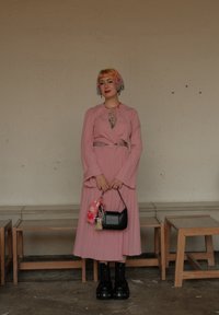 Larga vestido plisado rosa con mangas acampanadas y un cinturón plateado. Bolso negro con llaveros y botas de plataforma gruesas negras.