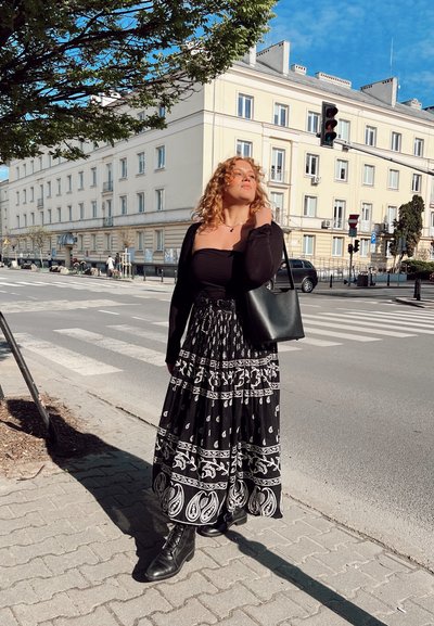 Falda larga de patrón blanco y negro con volantes, combinada con una blusa negra y un cárdigan. Botas de combate negras y un bolso de hombro completan el conjunto.