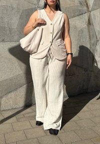 Žvakiškai pilkos spalvos be rankovių liemenė su vertikaliomis juostelėmis ir mygtukais, kombinuota su laisvomis, derančiomis juostuotomis plataus kirpimo kelnėmis ir juodais bateliais.