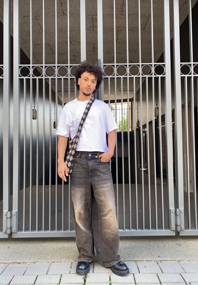 Conjunto informal que incluye una camiseta blanca, jeans wide-leg negros desgastados y zapatos de plataforma negros. Accesorios con una correa de hombro a cuadros.