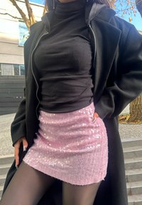 Schwarzer, gerippter Rollkragenpullover kombiniert mit einem pinken Minirock aus Pailletten. Der Rock weist eine strukturierte Oberfläche und einen leicht ausgefransten Saum auf.