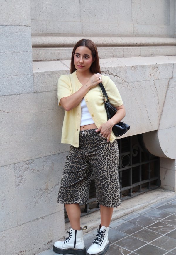 Lys gul kortærmet cardigan, hvid crop top, leopardmønstret bredbenede bukser og hvide snørebåndsstøvler med sorte såler. Sort håndtaske.