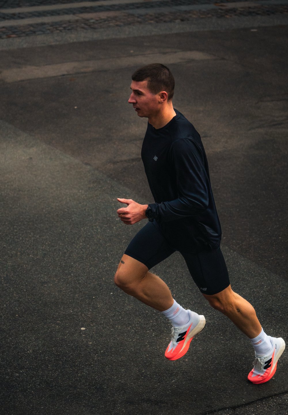 Homme en tenue de sport noire et chaussures de course brillantes courant sur une route en asphalte.