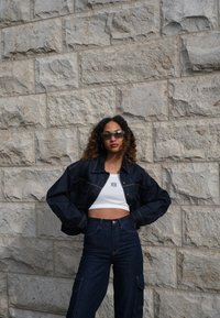 Denim jacket with a relaxed fit, contrasting stitching, and oversized sleeves, teamed with high-waisted dark denim cargo trousers and a white cropped top.