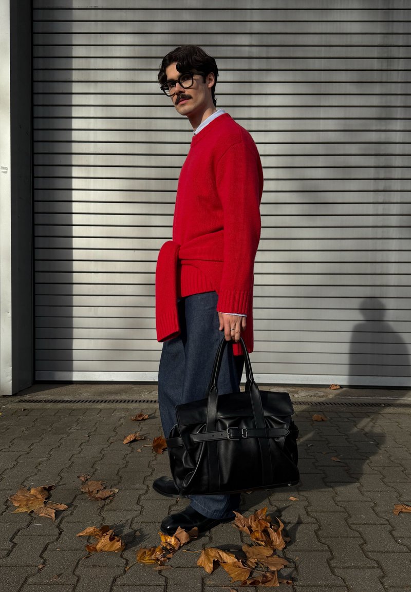 Pull en maille rouge, larges poignets et lien à la taille, associé à un pantalon large en jean foncé. Sac en cuir noir avec double poignée et détail boucle.