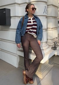 Denim bomber jacket, polo maroon dan putih bergaris, celana flare bergaris coklat, dan sepatu platform dengan sol kayu dan bagian atas merah tua.