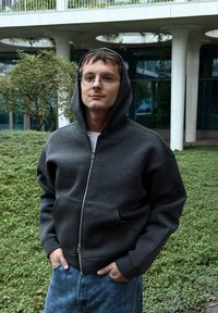 Pilka užtraukiama su gobtuvu su raišteliais, pasižyminti lygia faktūra ir šoninėmis kišenėmis, derinama su mėlynais raštuotais džinsais.