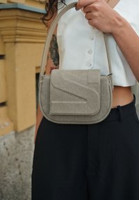 Borsa a tracolla beige testurizzata con una tracolla curvata e chiusura a patta, caratterizzata da un design impresso sul davanti.