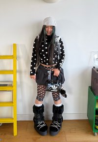 Musta pallokuvioinen pitkähiha-paita, musta hame, kuvioidut leggingsit, mustat karvaiset saappaat ja pieni musta käsilaukku valkoisella logolla.