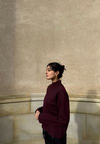 Bordeauxrode trui met een col, geribbelde manchetten en een losse pasvorm, gecombineerd met zwarte stoffen broek. Eenvoudig ontwerp, zachte textuur.