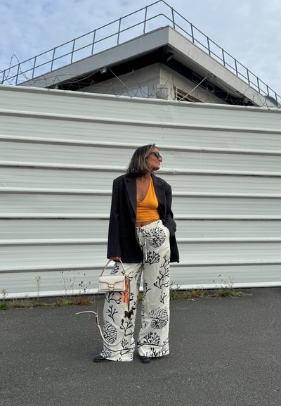Blazer negro a rayas, top corto naranja y pantalones de pierna ancha con estampado floral blanco. Accesorios incluyen un pequeño bolso blanco y gafas de sol.