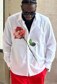 Chemise blanche à boutons avec un grand motif de rose rouge et feuilles vertes, assortie à un pantalon rouge. Texture lisse, col standard.