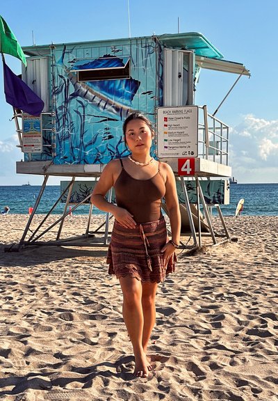 Joven caminando descalza por la playa de arena cerca de la torre de salvavidas con el océano y el cielo azul de fondo.