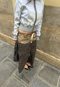 Grijs en groen kleurgebroken cropped sweatshirt met knoppen, gecombineerd met een tan en donker camo cargorok met zakken en trekkoord. Zwarte puntige schoenen.