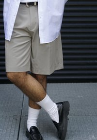 Šviesiai rudos šortai su laisva pritaikymu, derinami su baltais kojinėmis ir juodomis loafer'iais. Šviesios spalvos marškiniai dalinai uždengia šortus.
