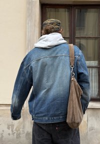 Jeansjacka med en bleknad blå nyans, grå huvtröja under, och en brun axelväska. Jackan har vida ärmar och sömnadsdetaljer.