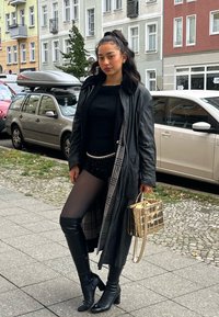 Czarna skórzana kurtka nałożona na czarną bluzkę i błyszczące szorty. Czarne rajstopy i kozaki do kolan. Metaliczna złota torebka z łańcuchowym akcentem.