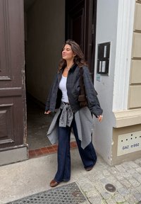 Črna in zelena karirana jakna čez belo majico, široke temno modre kavbojke in rjave čevlje. Karirana srajca zvezana okoli pasu.