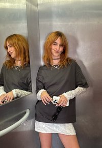 Labava siva majica s čipkastim dugim rukavima u kombinaciji s bijelom teksturiranom suknjom. Odsjaji su vidljivi u metalnom dizalu.