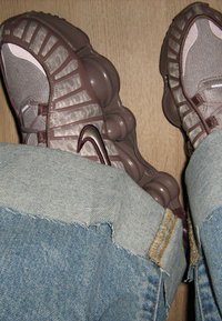 Nohy v hnědých teniskách Nike s bublinkovými podrážkami a světle modrých džínech s roztrhanými manžetami na dřevěné podlaze.