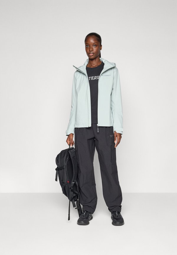Light blue, hooded waterproof jacket with zip front, paired with a black t-shirt and black cargo pants. Black backpack held in one hand.