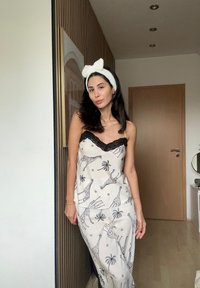 Naktiniai drabužiai be rankovių, kreminės spalvos su juodo nėriniu apvadu, turintys žirafų ir palmės medžių raštą, derinami su balta galvos juosta.