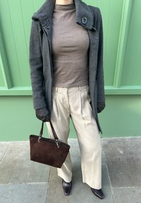 Manteau en laine gris avec col cranté et bouton, haut marron ajusté, pantalon plissé crème, sac à main en daim brun foncé et escarpins à bout pointu.
