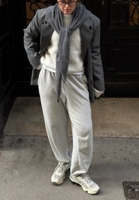 Blazer gris oversize porté sur un pull crème, pantalon de jogging gris et baskets gris clair. Textures douces et coupe ample définies par des tons neutres.