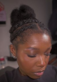 Kvinne med flettehår stylet i en knute, iført sølv øreringer i hoops og stift, ser nedover med lukkede øyne i et innendørs miljø.