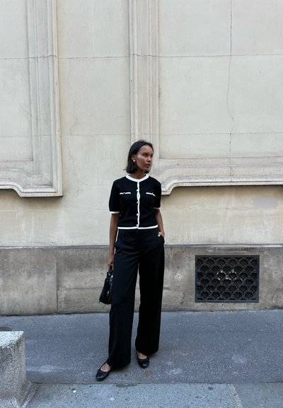 Top de punto negro con ribetes blancos, combinado con pantalones anchos negros. Los accesorios incluyen un bolso negro y zapatos planos. Texturas suaves en todo.
