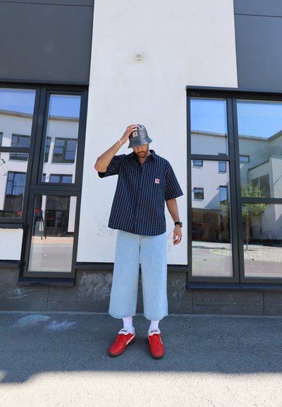 Camisa de rayas blancas y negras de manga corta, jeans de pierna ancha azul claro, sombrero de cubo gris y zapatillas rojas con detalles blancos.
