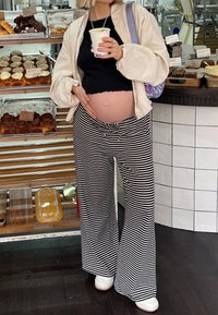 Μπλούζα με λευκό και μαύρο ριγέ παντελόνι σε φαρδιά γραμμή με κορδόνι στη μέση, συνδυασμένο με μαύρη μπλούζα και ένα oversized μπεζ σακάκι.