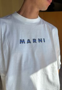 Camiseta de algodão branca com a palavra "MARNI" em letras negritas e listradas nas tonalidades de azul e preto ao longo do peito.