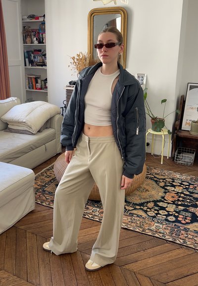 Chaqueta de plumas negra, top blanco corto, pantalones beige de pierna ancha y zapatos de color claro. Los accesorios incluyen gafas de sol estrechas y pendientes.