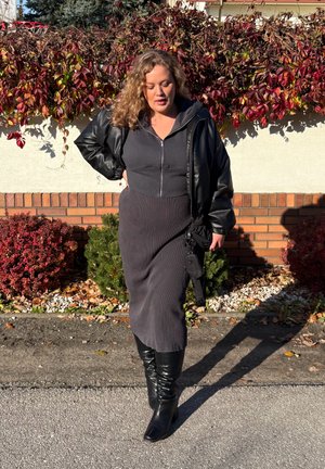 Vestido de canalé gris oscuro con cremallera frontal, combinado con una chaqueta de cuero negra oversize y botas negras hasta la rodilla. Los detalles incluyen un bolso pequeño.