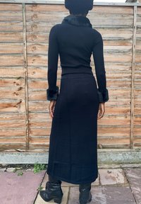 Čierny rebrovaný top s umelým kožušinovým golierom a manžetami, v kombinácii s priliehavou čiernou sukňou rovnakej farby, ktorá zdôrazňuje čistý, štíhly siluet.