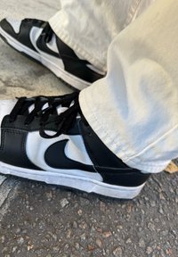 Schwarz-weiße Nike-Sneaker mit einem Obermaterial aus Leder und strukturierten Sohlen, ausgestattet mit einem markanten Logo und schwarzen Schnürsenkeln.