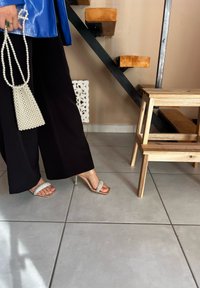 Μαύρο παντελόνι σε φαρδιά γραμμή, γυαλιστερό μπλε τοπ, ανοιχτά ψηλοτάκουνα παπούτσια με ασημί λεπτομέρειες, και τσάντα από μαργαρίτες με δομημένο τριγωνικό σχέδιο.