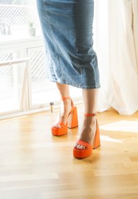 Orange platform sandaler med en kraftig blokhæl, der har ankelremme og åben tå, parret med en denimnederdel.