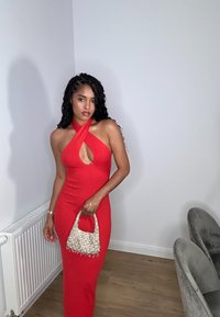 Vestido rojo ajustado con escote halter y corte en forma de llave. Acentuado con un bolso tejido color crema que presenta detalles de cuentas. Silueta curva.
