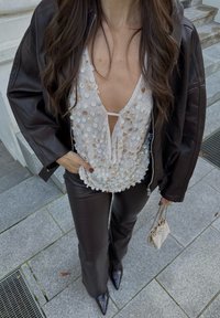 Ruskea nahkabomber-takki, joka on puettu kermaiseen yläosaan, jossa on pyöreitä paljetteja, yhdistetty tummiin istuviin nahkahousuihin ja kärjellisiin mustiin korkokenkiin.