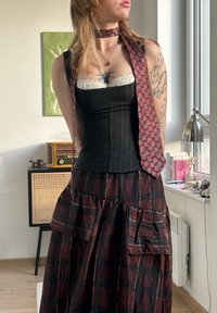 Sort og rødt ternet nederdel med lommer, lagdelt over en tætsiddende sort og hvid stribet top. Fremhævet med et mønstret rødt slips.