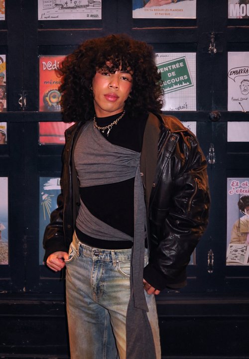 Veste en fausse fourrure dans des tons de marron, coupe oversized, portée avec un jean noir et des bottes en cuir marron. Tenant un sac à main en cuir noir.