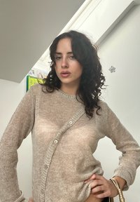 Cardigan de malha bege claro, com decote redondo, apresentando fecho com botões, mangas longas e um tecido suave e texturizado.