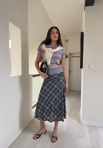 Top de punto a rayas en azul, rojo y verde, combinado con una falda cruzada gris de cuadros. Los accesorios incluyen un bolso negro y sandalias de tiras.