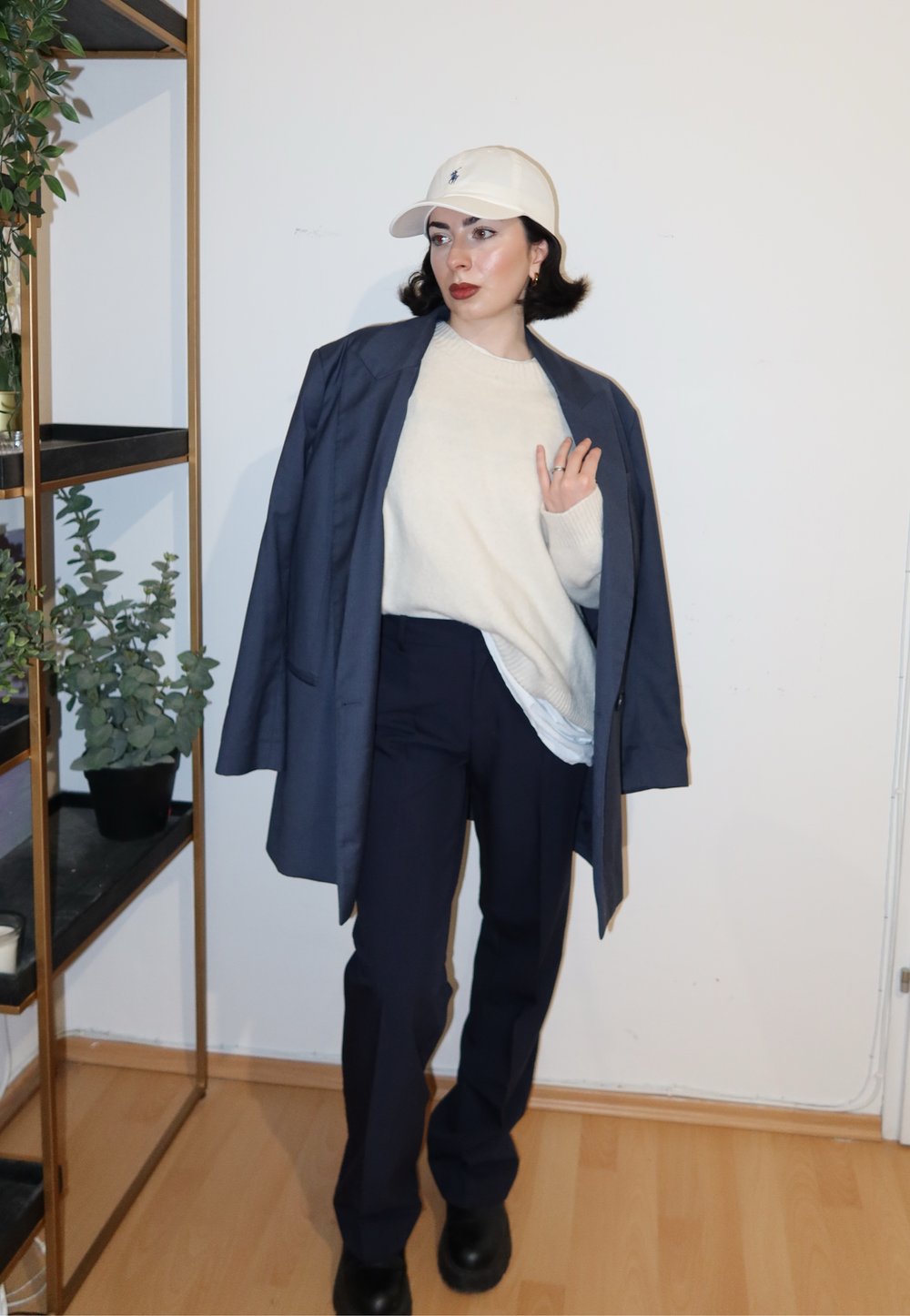Blazer bleu marine surdimensionné, pull crème, pantalon bleu marine et bottes noires. Casquette de baseball blanche pour ajouter du contraste. Design simple et minimaliste avec des tons neutres.